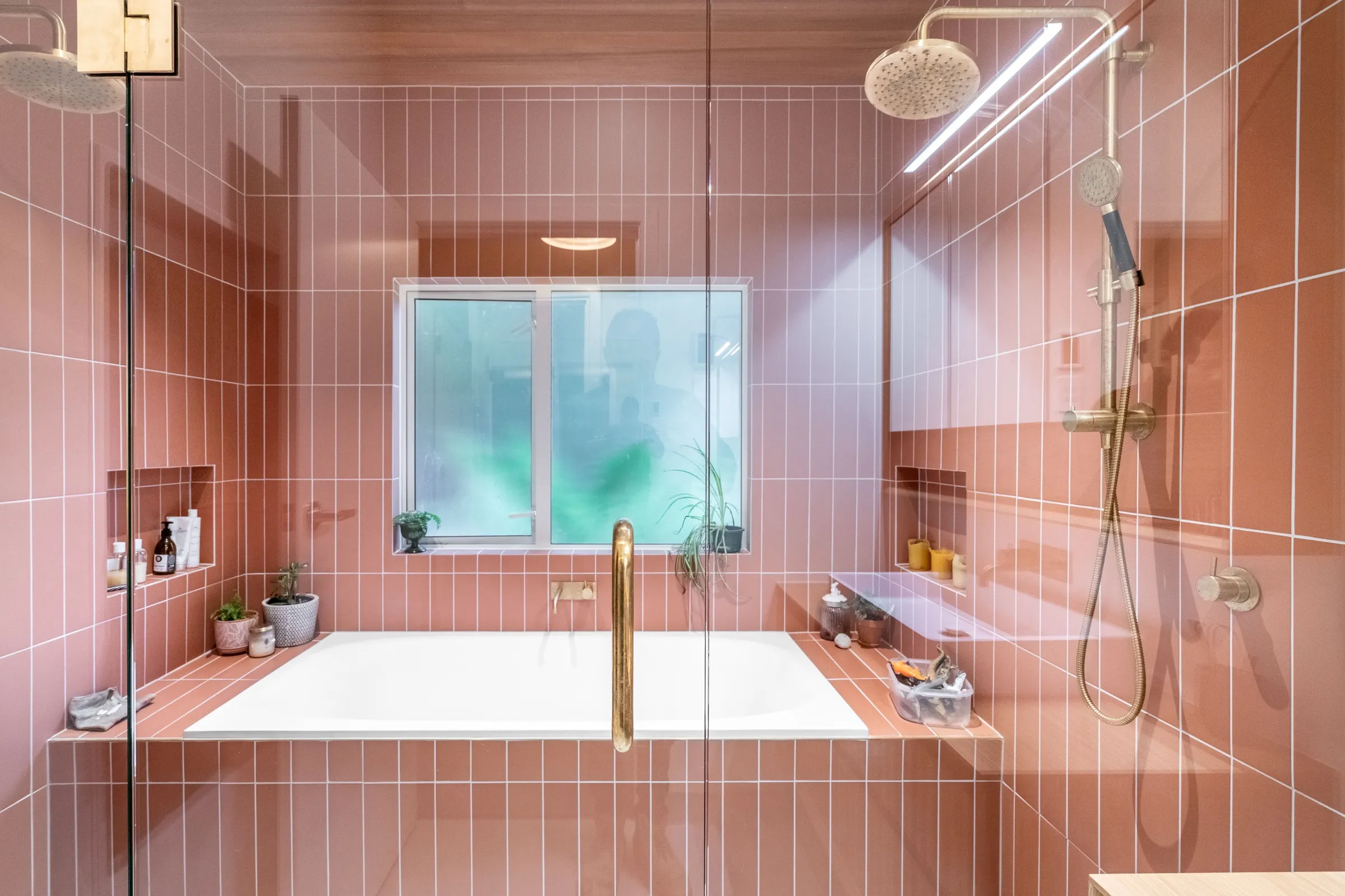 Completed bathroom with a tiled-in bath, brass tapware and a walk-in shower behind frameless glass