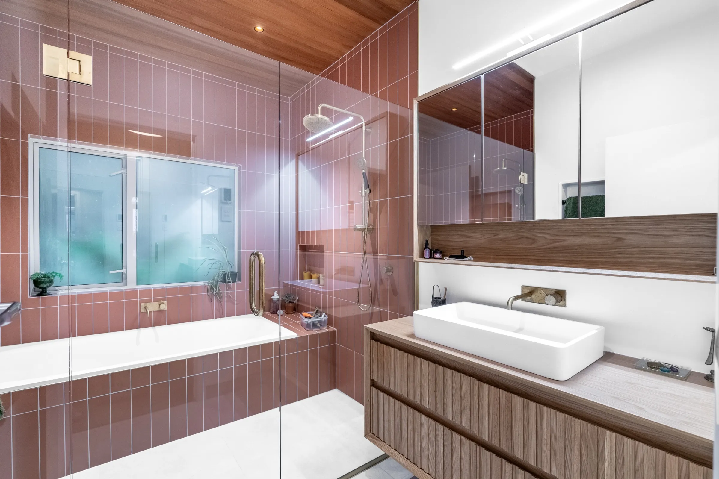 Completed bathroom renovation with blush vertical tiling, a cedar ceiling and a fluted timber vanity